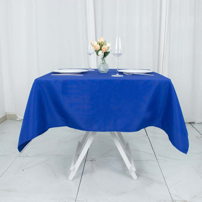Blue tablecloth on a dining table set for two with flowers and wine glasses.