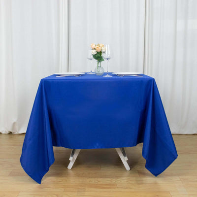 Blue tablecloth draped over a table with flowers and glasses on top.