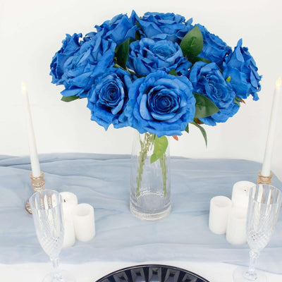 Blue rose bouquet in a glass vase with candles and elegant table setting.