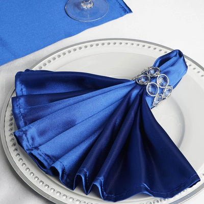 Elegant blue satin napkin with jeweled ring on a white plate.