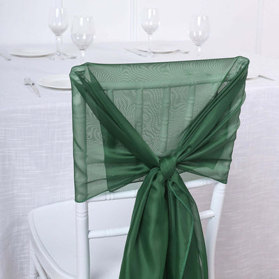 Green chair sash tied in a bow on a white chair at an elegant dining table.