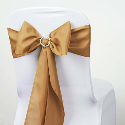 Gold satin chair sash with pearl ring detail on a white chair.