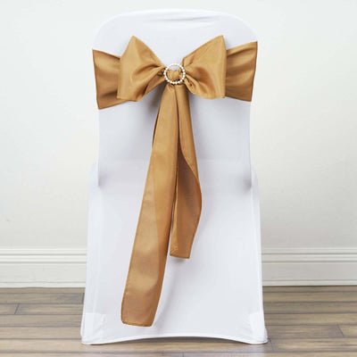 Gold satin chair bow with a decorative centerpiece on a white chair.