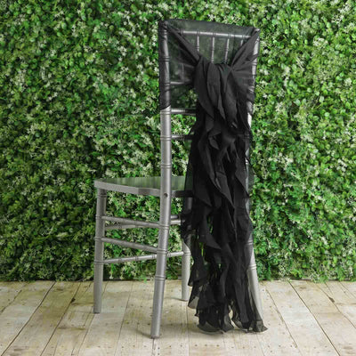 Silver chiavari chair with a black ruffled sash against a greenery backdrop.