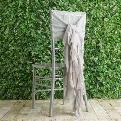 Silver chiavari chair with a draped light gray sash against a greenery backdrop.