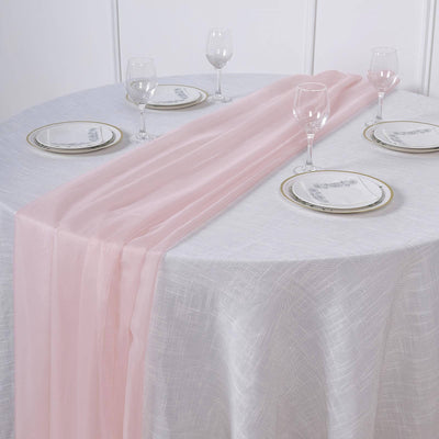 Pink table runner on a round table set with plates and glasses.