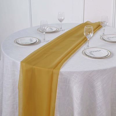 Gold table runner on a white tablecloth with elegant dinnerware set.