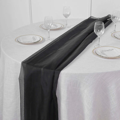 Black table runner on a white table set with plates and glasses.