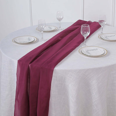 Burgundy table runner draped on a round table with elegant glassware and plates.