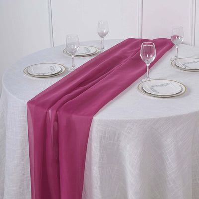 Pink table runner on a white tablecloth with plates and glasses set for dining.