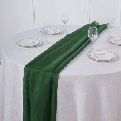 Green satin table runner on a white table with elegant dinnerware.