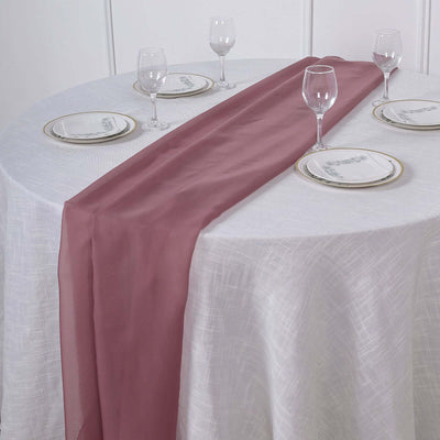 Elegant burgundy table runner on a white tablecloth with glassware and plates.
