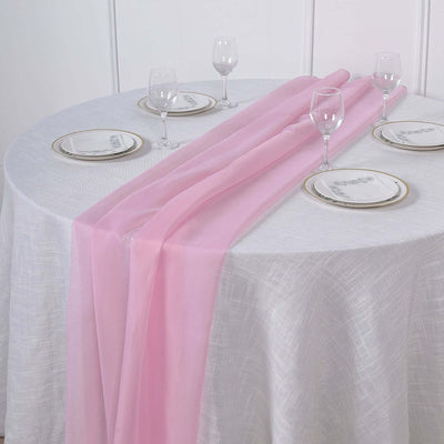 Pink sheer table runner elegantly draped over a white tablecloth with glassware and plates.