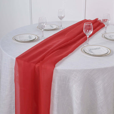 Red table runner on a white table with glassware and plates