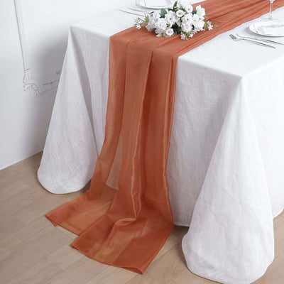 Elegant orange table runner on a white table setting with floral centerpiece.