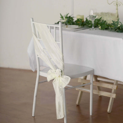 White chair with a draped satin ribbon and bow, set at a dining table.