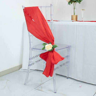 Clear chiavari chair adorned with a red sash and flower decoration.
