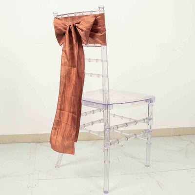 Clear Chiavari chair with a bronze satin bow on a plain backdrop.
