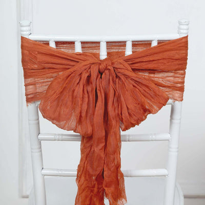 Rustic orange chiffon chair sash tied in a bow on a white chair.