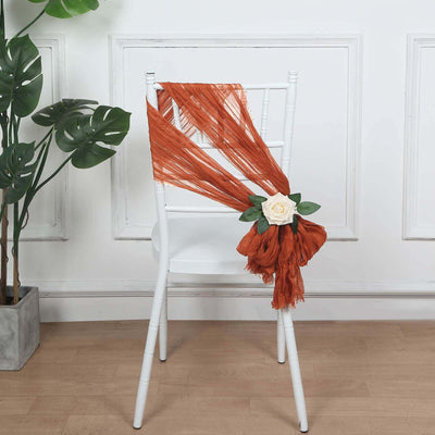 Rustic orange chair sash with rose accent on a white chair in a styled setting.