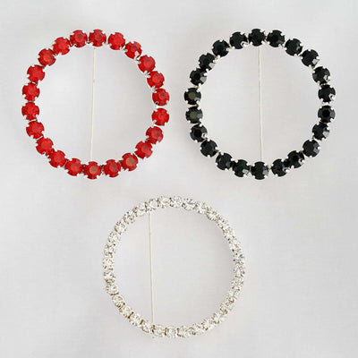 Three circular rhinestone brooches in red, black, and silver on a plain background.