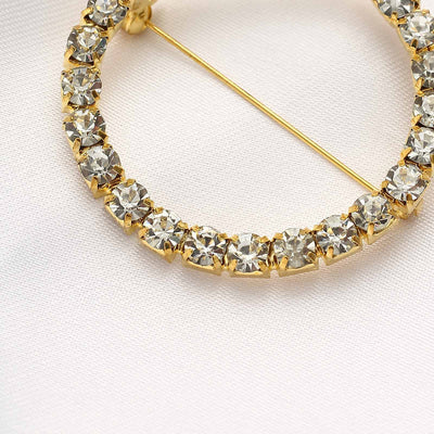 Gold hoop earring adorned with sparkling crystals on a soft fabric background.