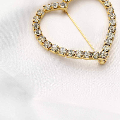 Gold heart-shaped brooch with sparkling rhinestones on a soft white fabric.