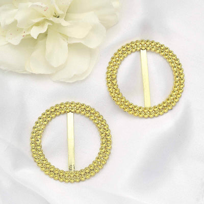 Gold circular hair clips with decorative beading on a soft fabric background.