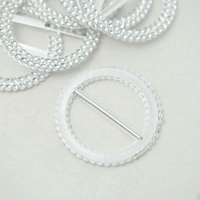 Silver circular brooch with beaded detailing on a light background.
