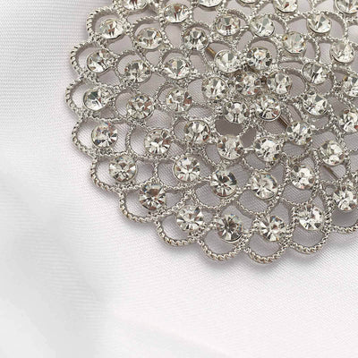Silver brooch with sparkling crystals on a white fabric background.