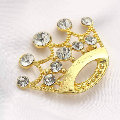 Gold crown brooch with rhinestones on a soft fabric background.