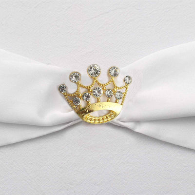 Gold crown brooch with rhinestones on a white fabric background.