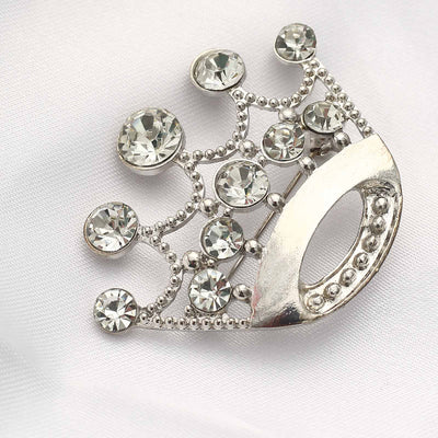 Elegant silver crown brooch with sparkling rhinestones on a soft fabric backdrop.