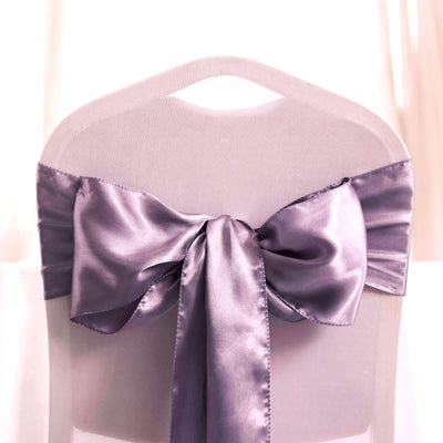 Purple satin chair sash tied in a bow on a clear chair.