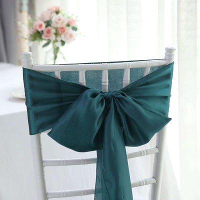 Teal satin chair sash bow tied on a white chair in a decorated setting.