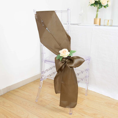 Brown satin chair sash with a flower decoration on a clear chair.
