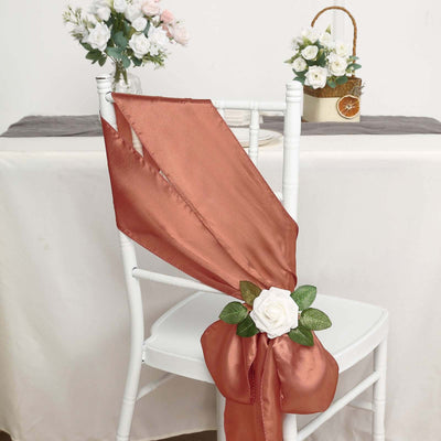 Rustic orange satin chair sash adorned with a white rose and greenery decoration.