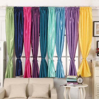 Colorful sheer curtains hanging in a bright room with a sofa and decorative items.