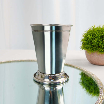Silver metal cup with decorative base on mirrored surface.