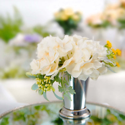 Elegant white flower arrangement in silver vase on reflective surface.