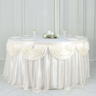Round table dressed in elegant ivory satin tablecloth with decorative draping.
