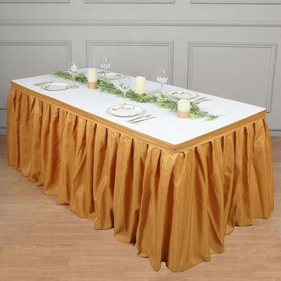 Elegant banquet table set with gold skirt, plates, candles, and greenery decor.