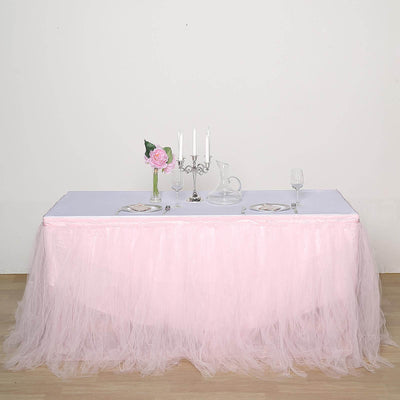 Elegant pink tulle table skirt draped over a white table setting with candles and flowers.