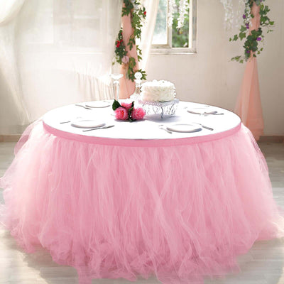 Pink tulle table skirt draped elegantly over a round table in a decorated setting.