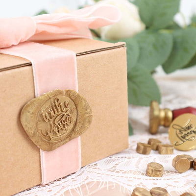 Gift box with gold seal and pink ribbon on lace tablecloth, surrounded by chocolates.