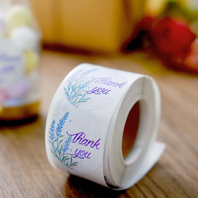 Roll of "Thank You" stickers featuring floral design on a wooden surface.