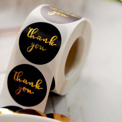 Roll of black and gold "thank you" stickers on a white background.