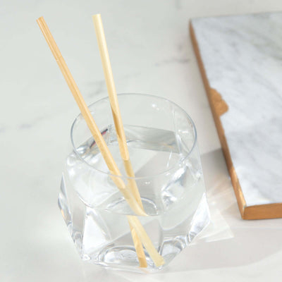 Clear glass with water and bamboo straws on a marble surface.