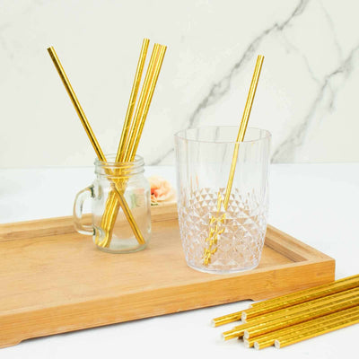 Gold metallic straws in a glass and jar on a wooden tray