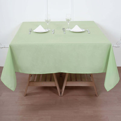 Green tablecloth on a wooden table set for dining with glasses and utensils.